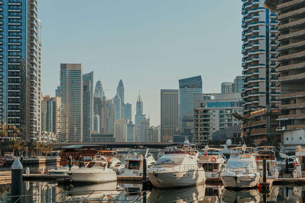 Waterfront line next to promenade in marina with luxury yachts and boats docked, modern high-rise buildings in background